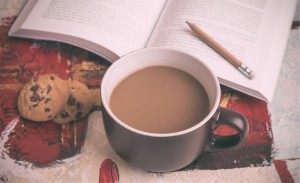 Dodatek do artykułu "20 cieplutkich piosenek na zimę". Przedtawia kubek z kawą i książkę z ołówkiem w tle, ułożone na świątecznym obrusie.