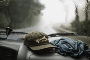 Dodatek do tekstu: "Ahoj przygodo! Podróże w pojedynkę". Zdjęcie przedstawia widok z przedniej szyby w samochodzie i leżące pod nią: czapkę i chustę. Za oknem widać drogę, po lewej stronie - las. Wszystko otulone jest mgłą.