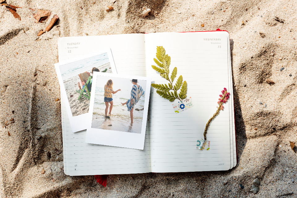 Dodatek do tekstu o tym, jak ułatwić sobie życie na studiach. Przedstawia brulion - leżący na piasku- z pamiątkami - zdjęciami z wakacji i zasuszonym liściem.